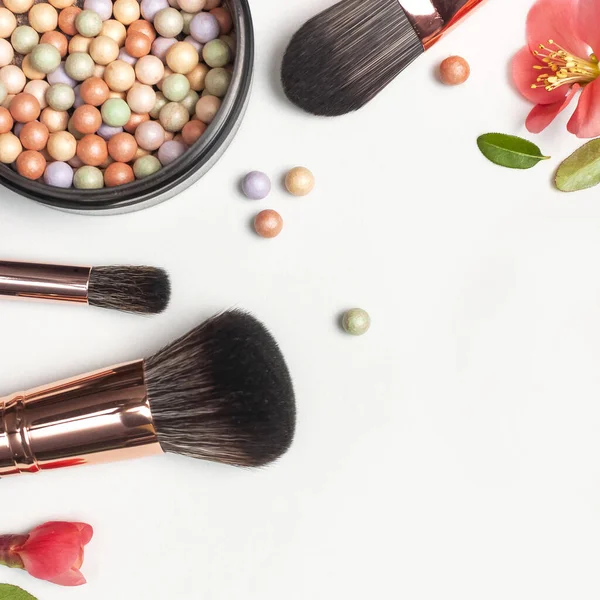 Professional makeup brushes powder blush balls with pink spring flowers on light background flat lay top view copy space. Beauty product, makeup, womens accessory, fashion. Cosmetic makeup Set