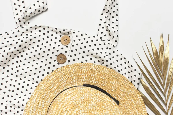 Летние женщины белое платье в черном горошек с натуральными деревянными пуговицами соломенная шляпа золотой пальмовый лист на светлом фоне. Плоское пространство для копирования сверху. Женская пляжная мода, летний стильный сарафан — стоковое фото