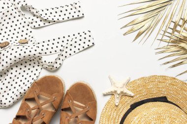 Yaz kadınlarının beyaz elbisesi siyah bezelye rengi sandaletler hasır şapka altın palmiye yaprağı kabuklar açık arkaplanda deniz yıldızı. Düz görünüm kopyalama alanı yatıyordu. Kadınların plaj modası tatil tatili altın gölgeler