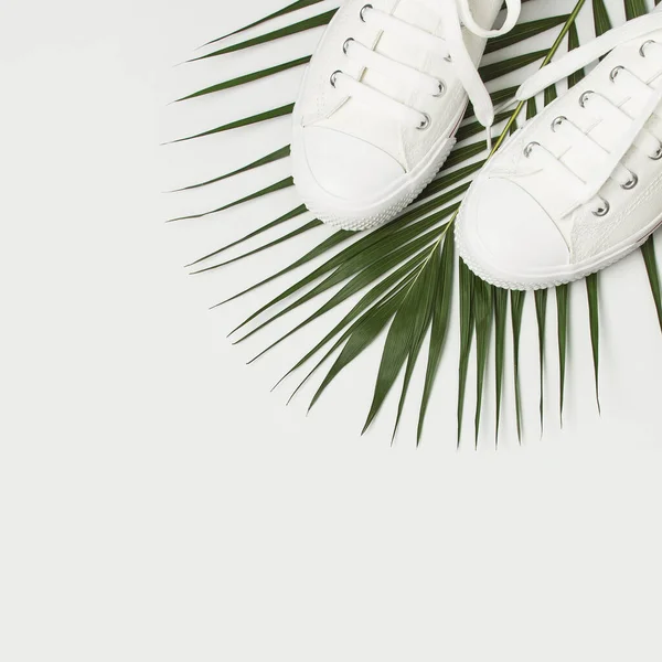 Witte vrouwelijke mode sneakers, tropische bladeren op lichtgrijze achtergrond. Flat lay bovenaanzicht kopieerruimte. Damesschoenen, accessoires. Stijlvolle witte sneakers. Creatief zomerconcept — Stockfoto