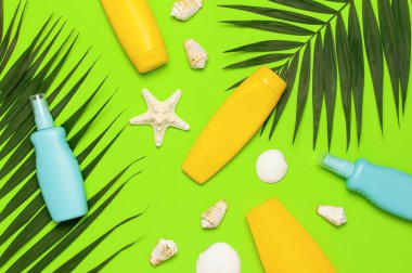 Güneş koruması Yaz tatili konsepti Sarı mavi güneş kremi şişeleri tropikal palmiye yaprakları yeşil arka planda deniz yıldızları düz görünüm fotokopi alanı yatıyordu. Yaz kozmetikleri.