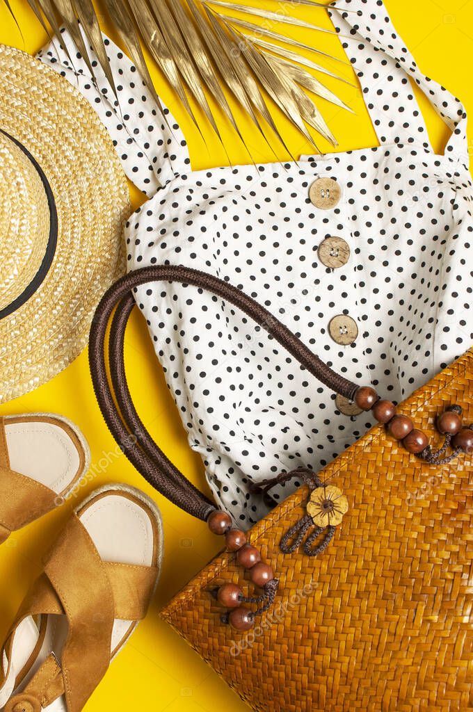 Beach wicker straw or rattan womens eco bag, white dress straw hat sandals golden tropical leaf on yellow background Flat lay top view copy space Concept of travel Summer background Beach accessories