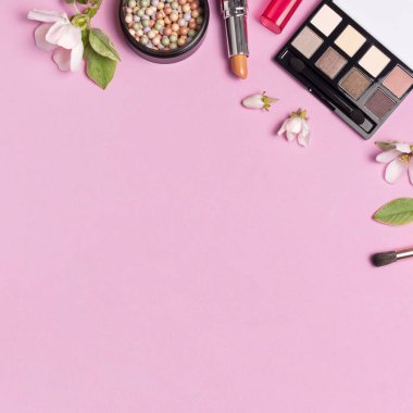 Dekoratif kozmetik maskara pudrası ruj göz farı, makyaj fırçası parfümü pembe arka planda bahar dalları, düz zemin. Güzellik blogcusu kavramı. Moda arkaplanı.