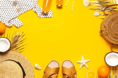 Yaz arkaplanı plaj aksesuarları. Plaj hasır hasır hasır örgü kadın eko çantası beyaz şapka sandalet altın tropikal yaprak Hindistan cevizi portakal suyu deniz yıldızı sarı arka planda. Düz üst görünüm.