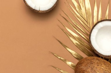 Hindistan cevizli yaratıcı düzen. Kahverengi arka planda tam ve yarım hindistan cevizi, altın palmiye yaprağı. En az düz konum biçimi, en üst görünüm kopyalama alanı. Yemek konsepti. Tropik egzotik meyve, yaz arkaplanı..