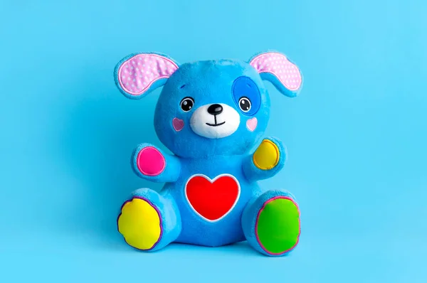 Azul suave niño juguete cachorro con orejas divertidas, patas multicolores y corazón rojo sobre fondo azul plano laico espacio de copia. Peluche perro de juguete, amigo del bebé, artículos de juego para niños, infancia feliz —  Fotos de Stock