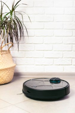Ev Temizliği Konsepti. Modern robot elektrikli süpürge, tuğla duvara karşı porselen fayanslardaki evleri temizliyor. Yeni teknolojiler, hızlı ev temizleme otomatik robot asistanı. Temizlik için akıllı aygıt.