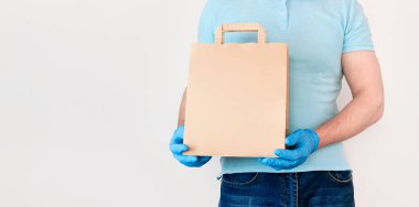 Coronavirus 2019-NCov 'a salgın hastalıklı Temassız Teslimat. Mavi eldivenli erkek, beyaz arka planda el işi kağıt torba tutuyor. Karantina sırasında yiyecek teslimatı kavramı.