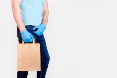 Coronavirus 2019-NCov 'a salgın hastalıklı Temassız Teslimat. Mavi eldivenli erkek, beyaz arka planda el işi kağıt torba tutuyor. Karantina sırasında yiyecek teslimatı kavramı.