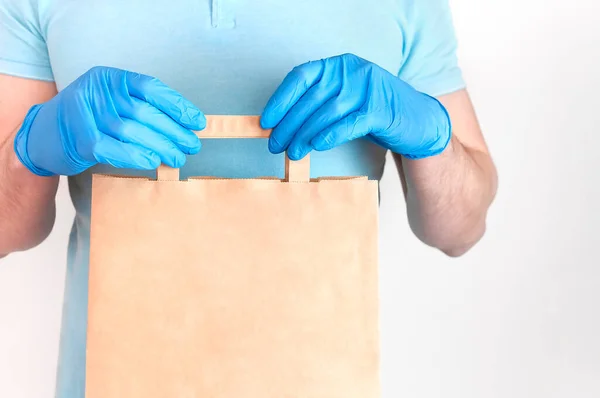 针对Coronavirus 2019 Ncov的无接触分娩 蓝色医用手套的男性手拿着白色背景的手工纸袋 检疫期间运送食物的概念 — 图库照片