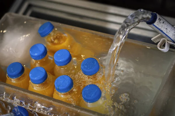 Orange juice bottles in the box with cold water. Cooling down with a jet of ice water.