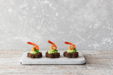 Avokado köpüklü kanepeler ve kahverengi ekmeğin üzerinde baharatlı karides.