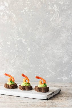Avokado köpüklü kanepeler ve kahverengi ekmeğin üzerinde baharatlı karides.