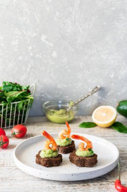Avokado köpüklü kanepeler ve kahverengi ekmeğin üzerinde baharatlı karides.