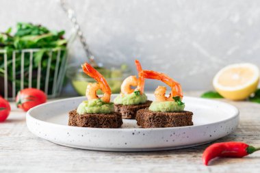 Avokado köpüklü kanepeler ve kahverengi ekmeğin üzerinde baharatlı karides.