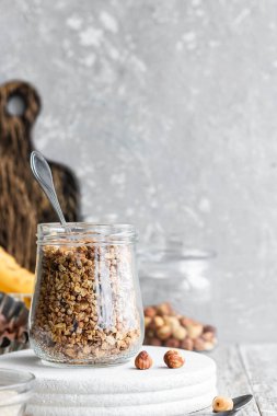 Chocolate banana granola with nuts in a glass jar on a light background