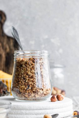 Chocolate banana granola with nuts in a glass jar on a light background
