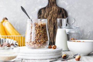Chocolate banana granola with nuts in a glass jar on a light background