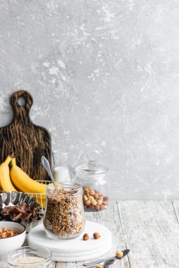 Chocolate banana granola with nuts in a glass jar on a light background