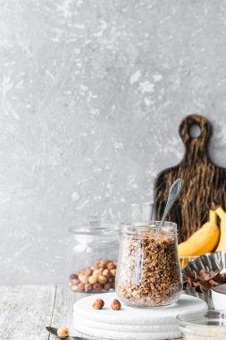 Chocolate banana granola with nuts in a glass jar on a light background