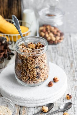 Chocolate banana granola with nuts in a glass jar on a light background