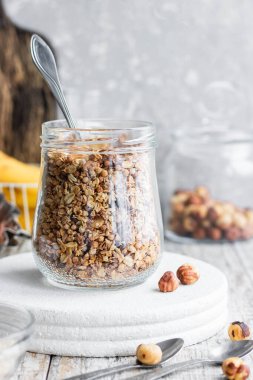 Chocolate banana granola with nuts in a glass jar on a light background