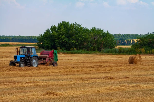 トラクターは夏の日に黄色い畑に大きな藁を転がし — ストック写真