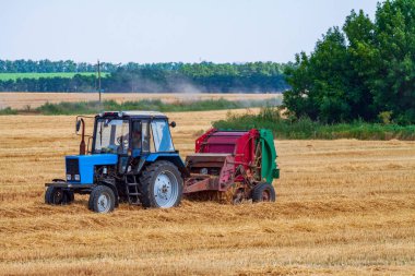 Traktör, yaz günü sarı alanda büyük saman rulosu yapar.