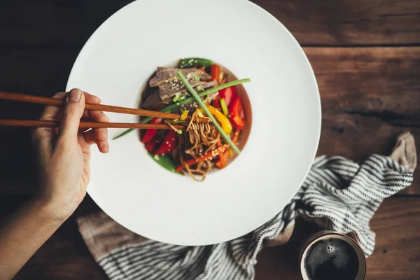 Woman eating noodles with meat and vegetables