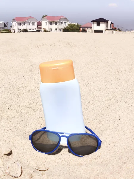 Bottle of balm solar with shells and sunglasses on sand