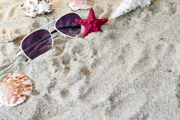 Sur le sable se trouvent des coquillages, une étoile de mer rouge et des lunettes de soleil. Concept d'été — Photo