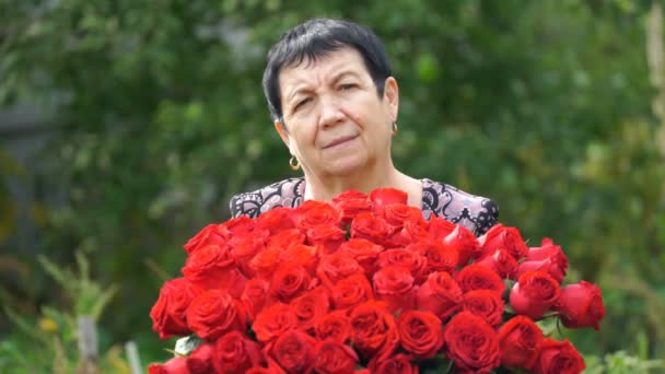 映像屋外にバラの花束を保持している年配の女性。4 k — ストック動画