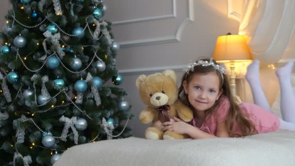 Vrouw ligt op bed met een teddybeer in de buurt van een kerstboom — Stockvideo