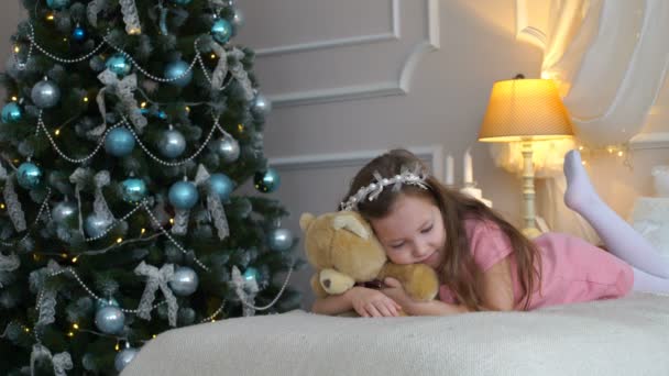 Woman lies on a bed with a teddy bear near a Christmas tree — Stock Video