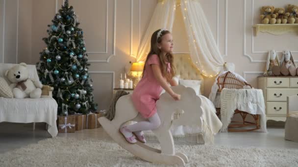 Una chica montando un caballo de juguete cerca del árbol de Navidad. 4K — Vídeos de Stock