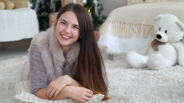 Mulher filmagem encontra-se em um tapete com um ursinho de pelúcia perto de uma árvore de Natal. 4k — Vídeo de Stock