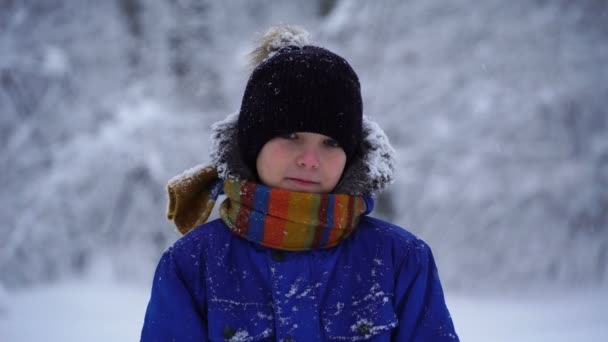 Pojke stående utanför i snöiga väder och ser in i kameran. — Stockvideo