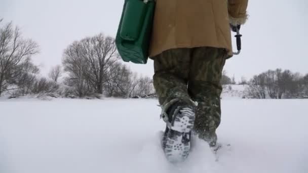 En fiskare går på en snötäckt sjö på jakt efter en bra fiskeplats. — Stockvideo