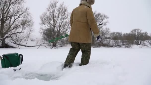 En fiskare går på en snötäckt sjö på jakt efter en bra fiskeplats. — Stockvideo