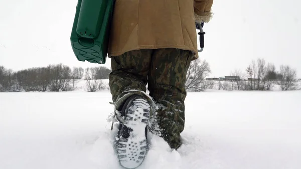 Un pescador camina sobre un lago cubierto de nieve en busca de un buen lugar de pesca . — Foto de Stock