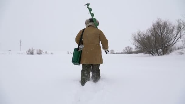 Un pêcheur marche sur un lac enneigé à la recherche d'un bon lieu de pêche . — Video