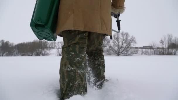 Een visser loopt op een besneeuwde meer op zoek naar een goede visserij plaats. — Stockvideo