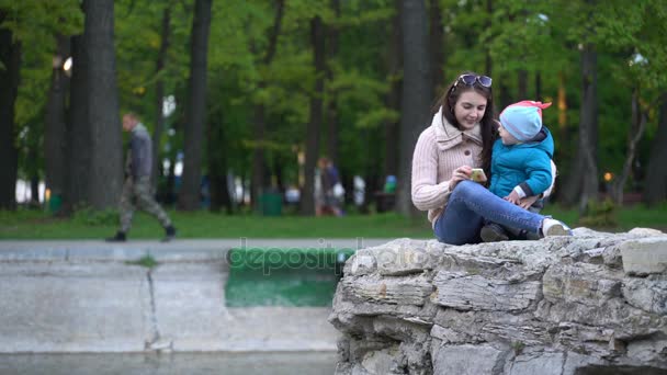 Mamá y su hijo en el parque viendo dibujos animados en un teléfono inteligente . — Vídeos de Stock