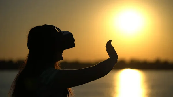 Frau mit Virtual-Reality-Brille auf dem Hintergrund des Sonnenuntergangs. — Stockfoto
