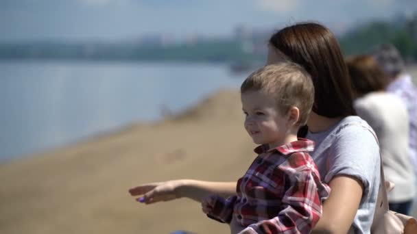 Anya és fia keres előre a vízparton. — Stock videók