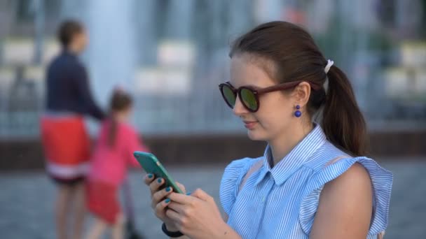 Flickan skriver ut text på sin smartphone medan promenader i parken. — Stockvideo