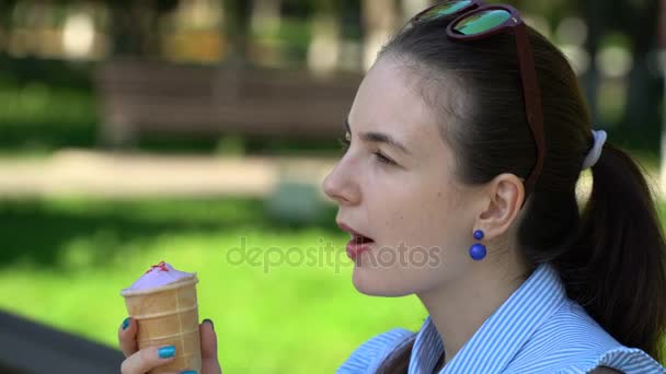 공원 벤치에 앉아 아이스크림을 먹는 여자. — 비디오