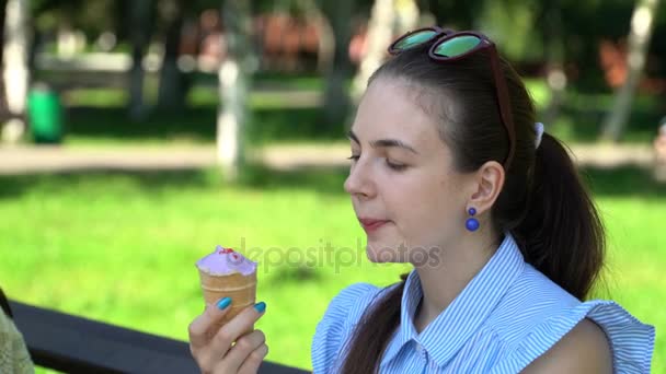 Menina comendo um sorvete sentado em um banco de parque . — Vídeo de Stock