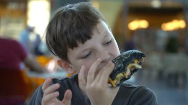 Oğlan siyah hamburger yiyor ve giysi smear.