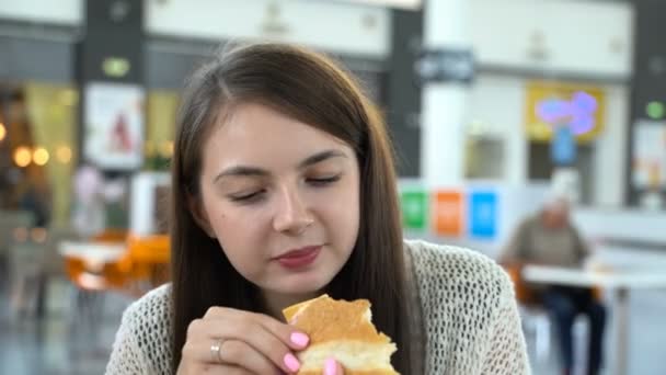 La ragazza sta mangiando un hamburger in una mensa. . — Video Stock